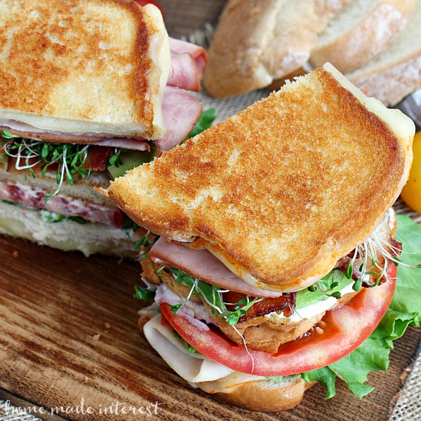 An amazing grilled cheese recipe for National Grilled Cheese Month! We’ve taken a California Club sandwich and turned it into a triple decker grilled cheese sandwich. This grilled california club sandwich oozes Munster cheese, and is piled high with ham, turkey, bacon, avocado, lettuce, tomatoes, and sprouts.