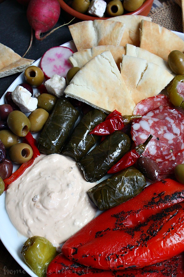 This easy antipasto platter is going to be a hit at your next party. A mediterranean antipasto platter filled with peppers, dolmas, meats, olives, and cheeses, served with flavored greek yogurts and pita bread, makes the perfect appetizer for a party.