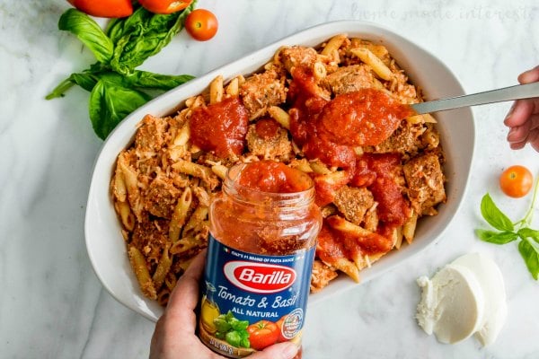 pouring Barilla tomato & basil pasta sauce on top of a chicken parmesan casserole