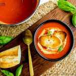 A top down photo of roasted red pepper soup topped with toasted baguettes.