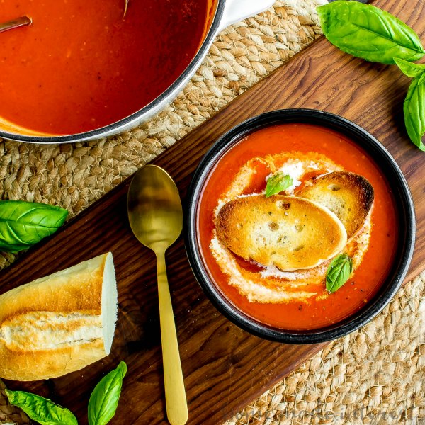 A top down photo of roasted red pepper soup topped with toasted baguettes. 
