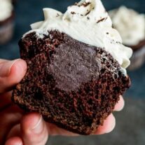 A person holding a chocolate cupcake with a bite out of it.