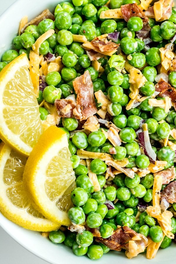 Close-up of Creamy Bacon Pea Salad with bright green peas, bacon, red onions, and lemon slices