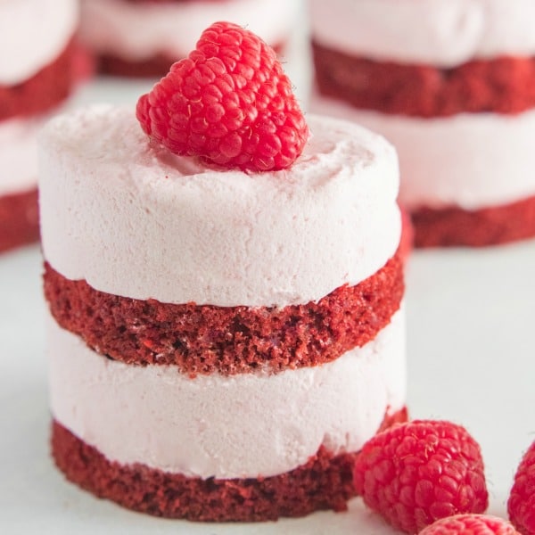 A beautiful mini raspberry mousse red velvet cake with raspberry mousse and red velvet cake layers topped with a fresh raspberry.