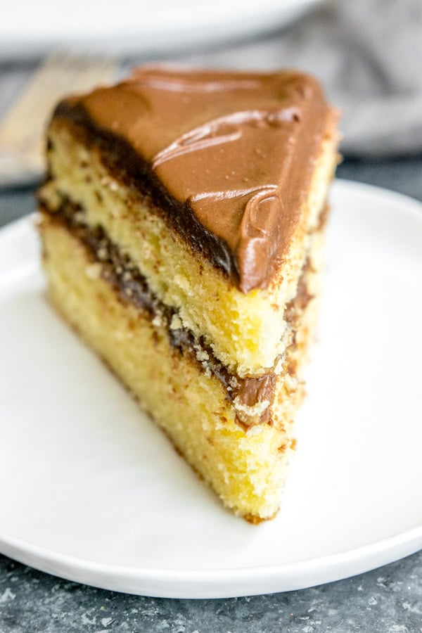 A big slice of yellow butter cake with chocolate frosting on a white plate