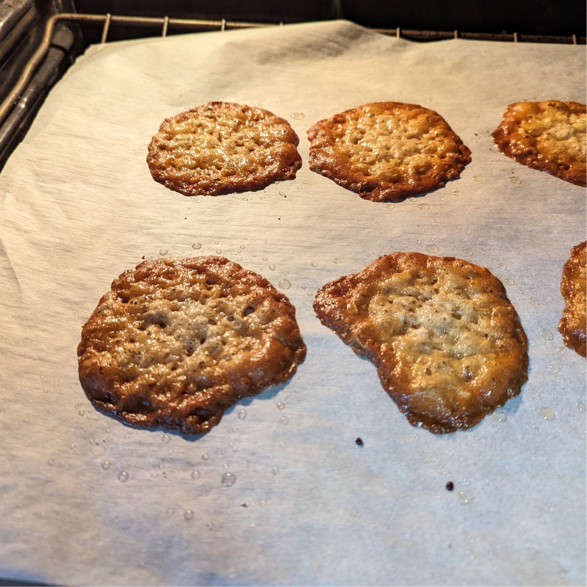 A tray of coconut oatmeal lace cookies on a baking sheet in the oven.