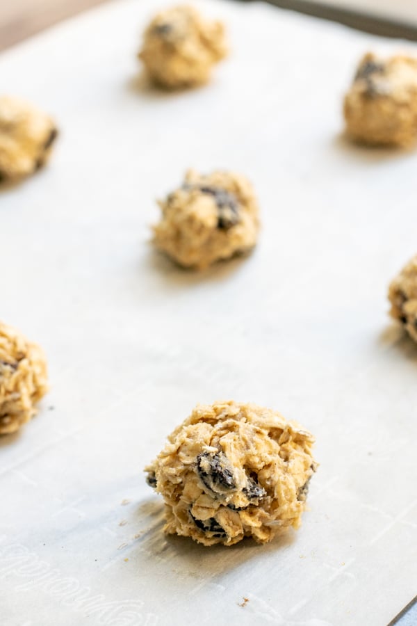 balls of chewy oatmeal raisin cookie dough sitting on a baking sheet