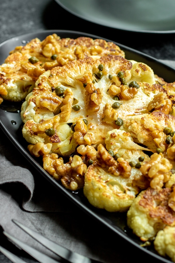 Several roasted cauliflower steaks with brown butter fanned out on a black plate