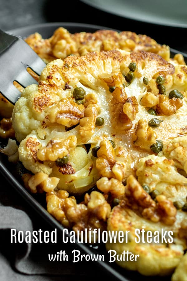A fork lifting a piece of roasted cauliflower steaks with toasted walnuts, capers, and brown butter