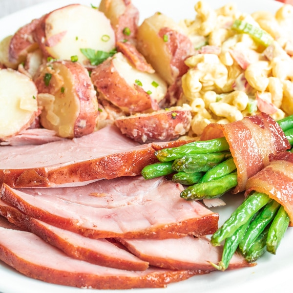 Easter dinner plate filled with honey glazed ham, green bean bundles, potato salad, and macaroni salad. 