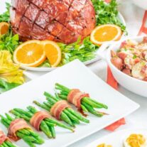 A festive meal spread featuring a glazed ham centerpiece, green beans wrapped in bacon, deviled eggs, and various salads.