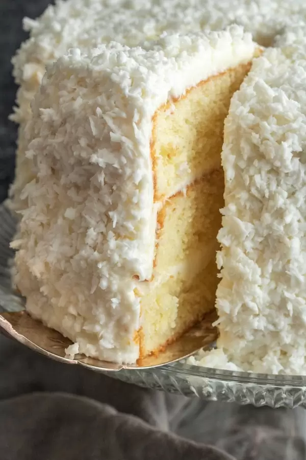 Slice of coconut cake being cut from a three layer coconut cake