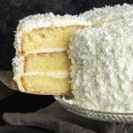 Slice of coconut cake being cut from a three layer coconut cake