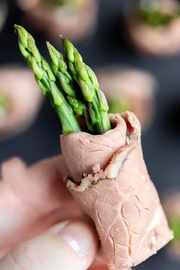 A hand holding appetizer sized Roast Beef and Asparagus Roll Ups