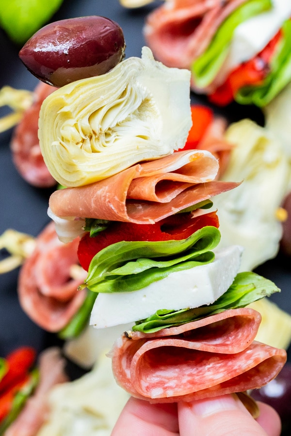 Hand holding antipasto skewer with layers of meat, cheese, and vegetables