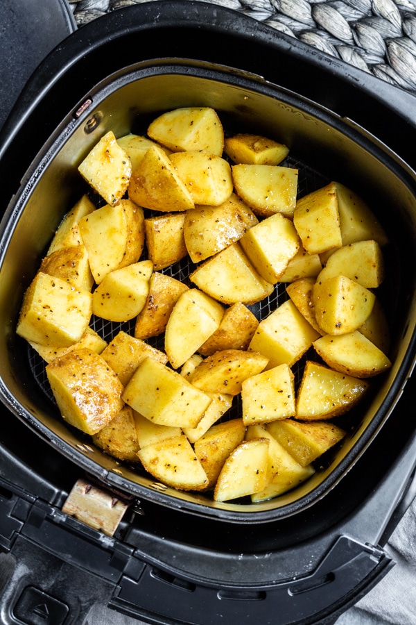air fryer basket with raw cubed potatoes