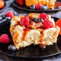 Overnight French Toast Bake on a black plate with fruit syrup and fresh berries