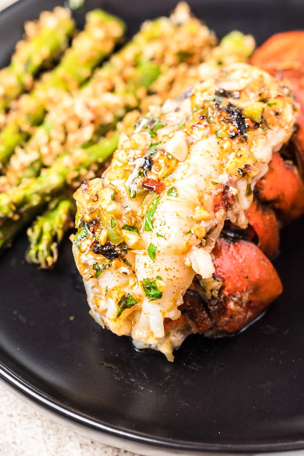 Broiled Lobster Tail on a black plate with asparagus