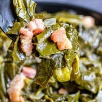 A spoonful of collard greens and bacon in a skillet.