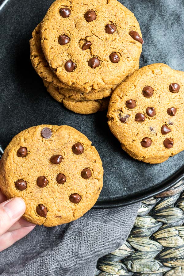 holding a Keto Peanut Butter Cookies with Chocolate Chips next to a stack of cookies