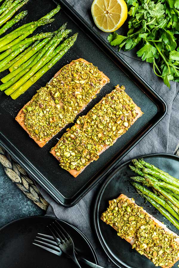 Two pieces of pistachio crusted salmon on a black sheet pan