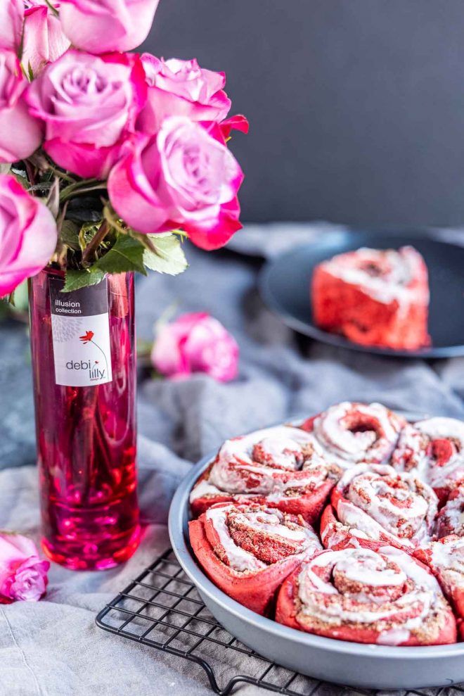 pink roses in a vase with a pan of Red Velvet Cinnamon Rolls