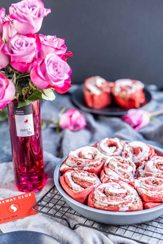 Red Velvet Cinnamon Rolls in a pan with a vase of roses and a Safeway card