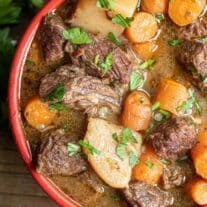 Beef stew in a red bowl with carrots and parsley.