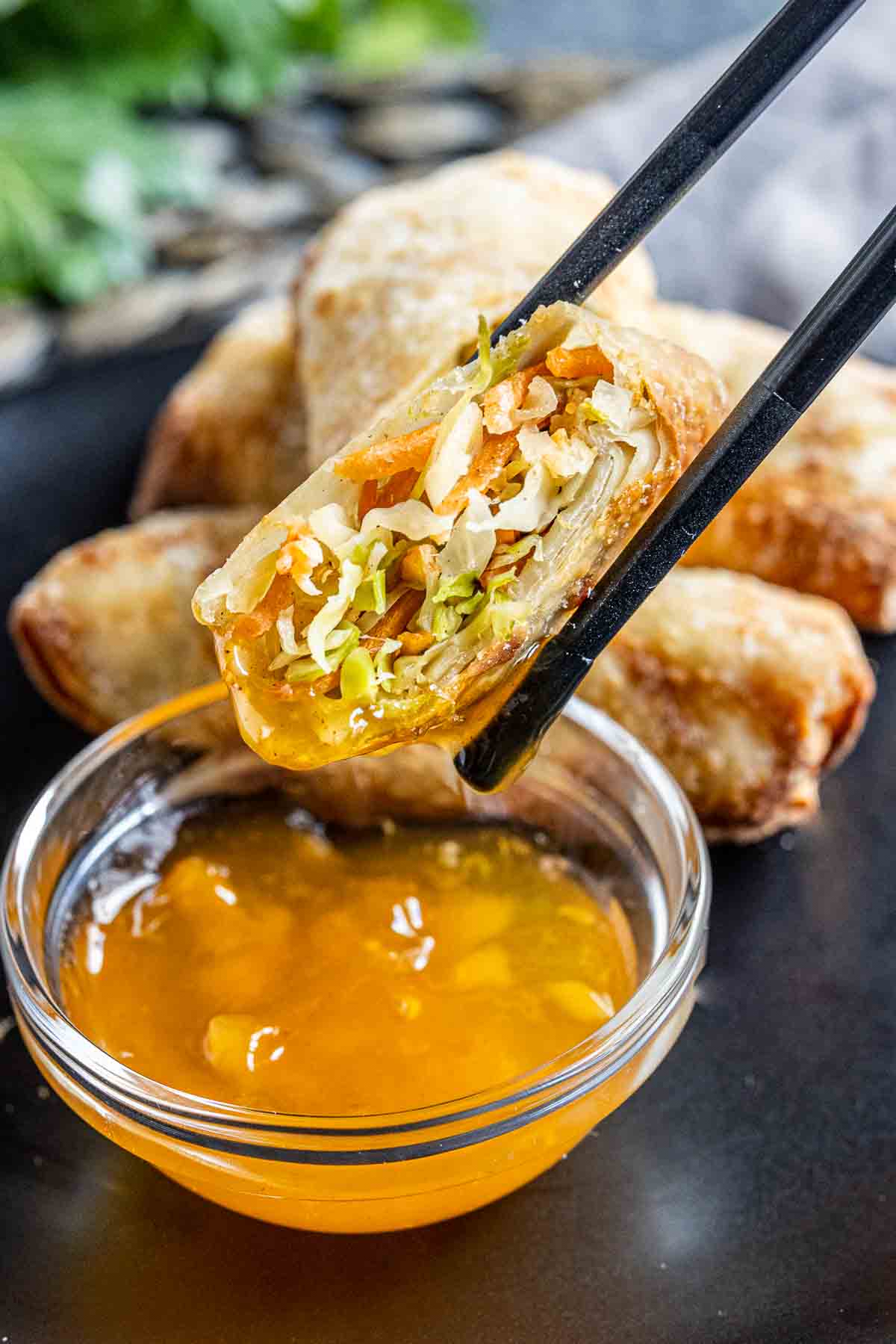 Chopsticks holding an egg roll and dipping Air Fryer Egg Rolls in duck sauce