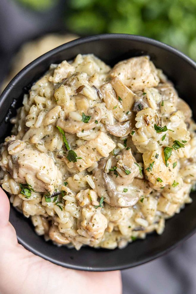 holding a black bowl of Instant Pot Cream of Mushroom Chicken and Wild Rice