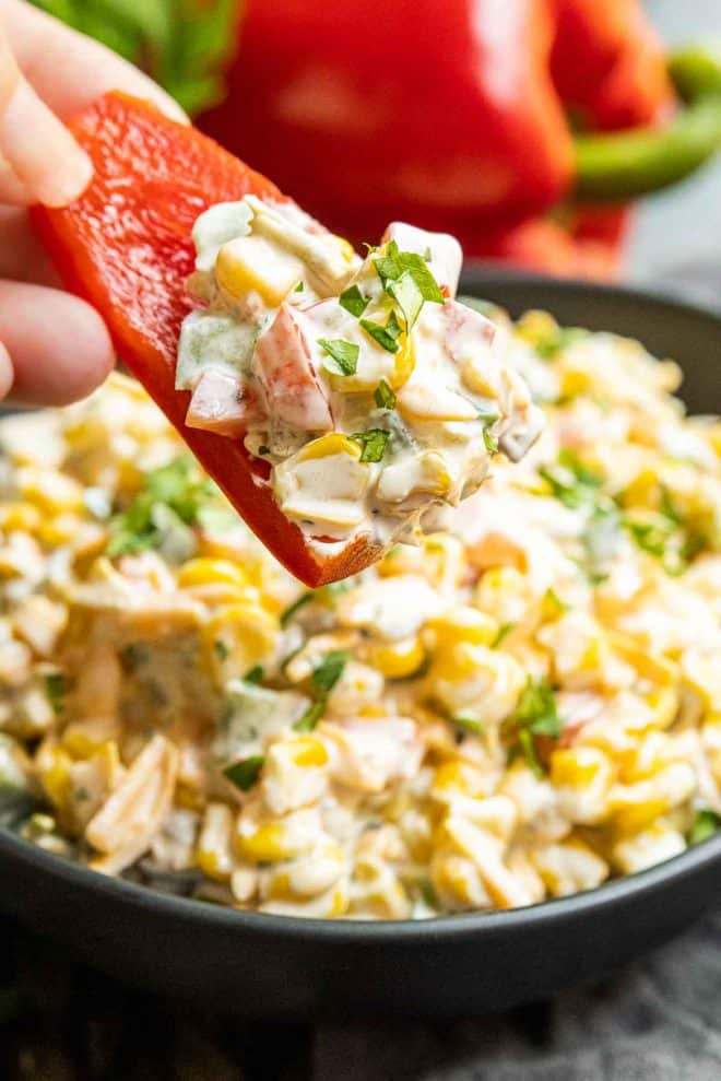 holding a red pepper slice with Creamy Jalapeno Corn Dip