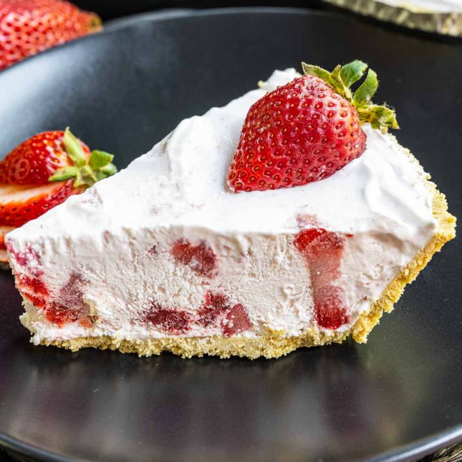 slice of Frozen Strawberry Pie on a black plate with fresh strawberries on top