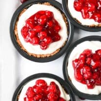 Four cherry pies topped with whipped cream and cherries.