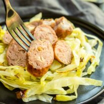 Sheet Pan Sausage and Cabbage on a plate with sausage on a fork
