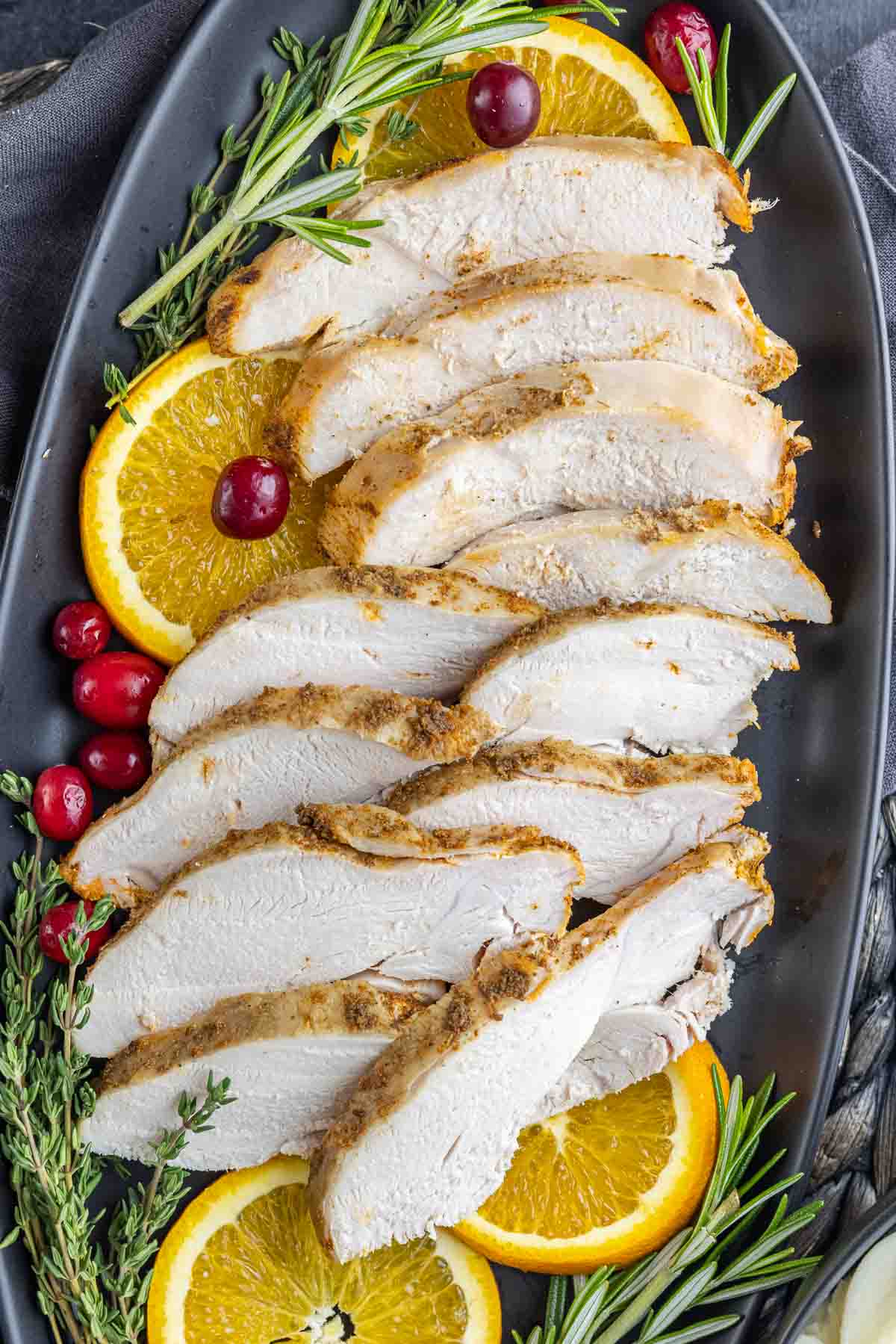 sliced Slow Cooker Turkey Breast with black platter with oranges, cranberries and rosemary