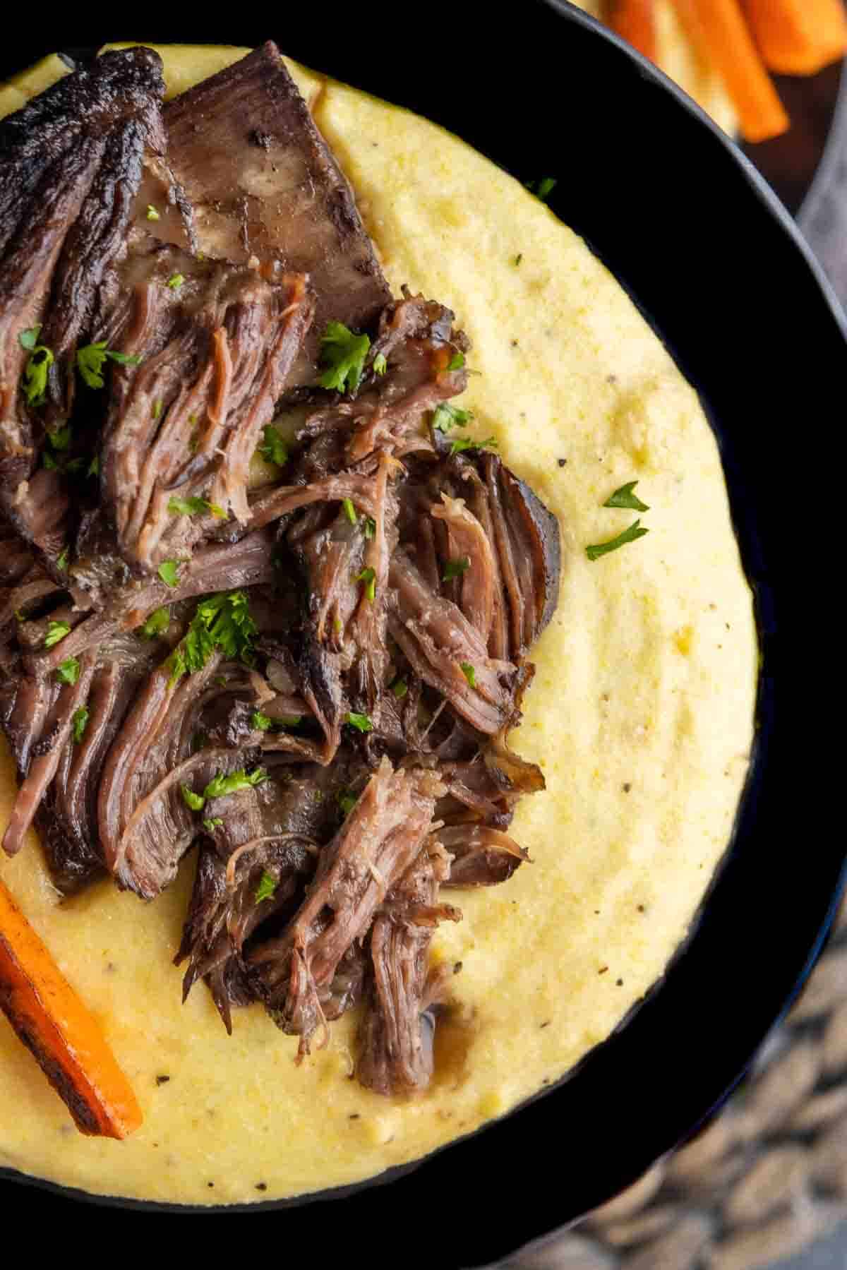 holding a plate of Creamy Polenta and braised ribs