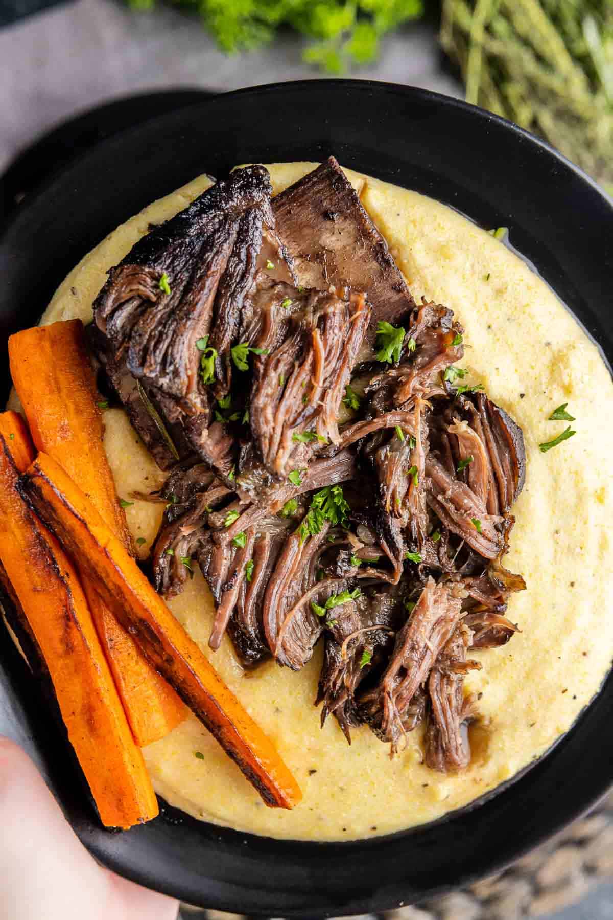 holding a plate with Red Wine Braised Short Ribs and polenta
