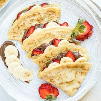 Nutella crepes with banana and strawberry on a white plate