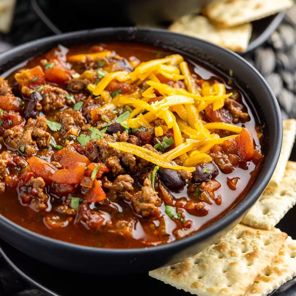 black bowl of Smoky Chipotle Chili topped with shredded cheese