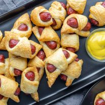 black platter of Air Fryer Pigs in a Blanket with yellow mustard on the side
