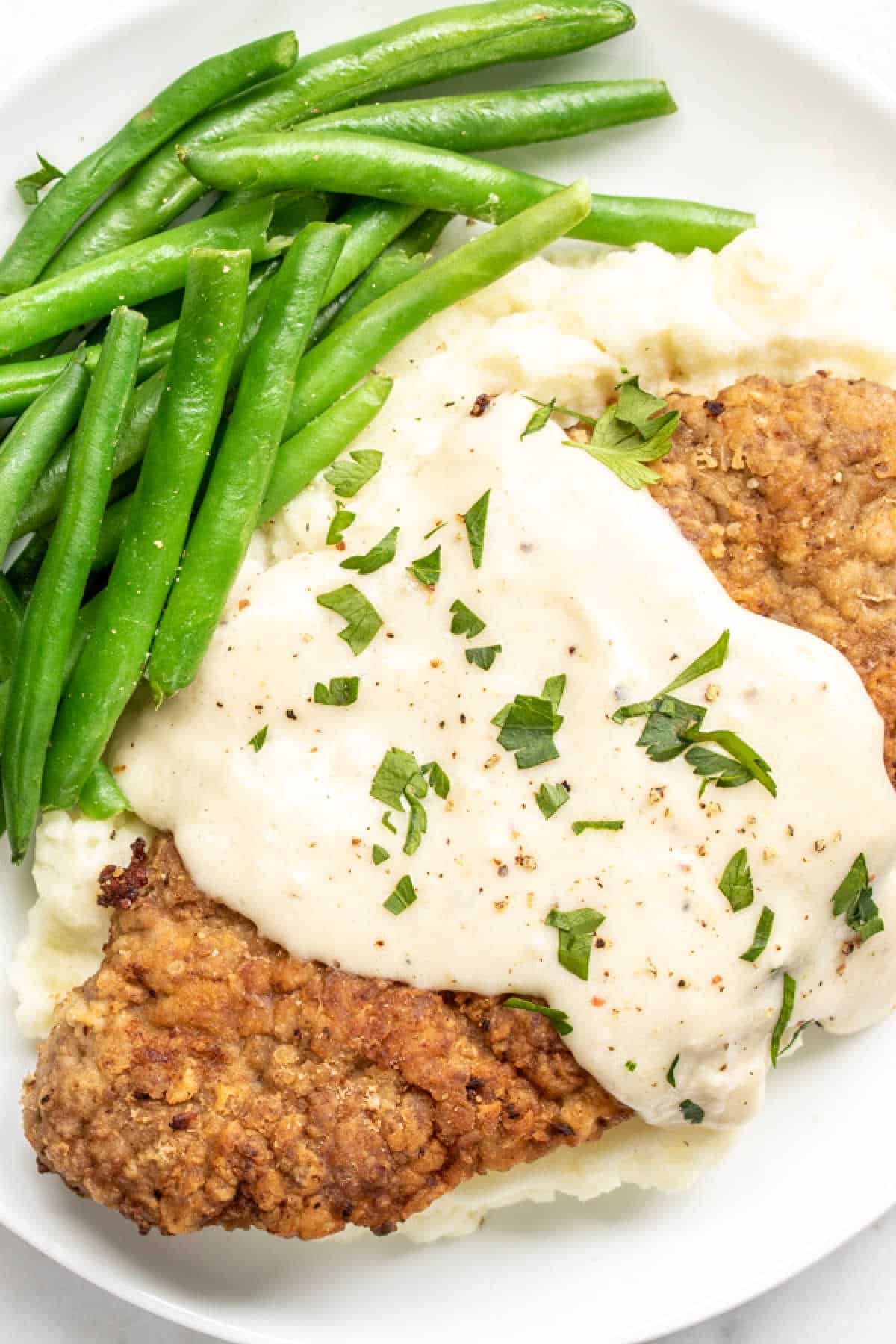 Chicken Fried Steak with Gravy on a hwote plate with green beans and mashed potatoes