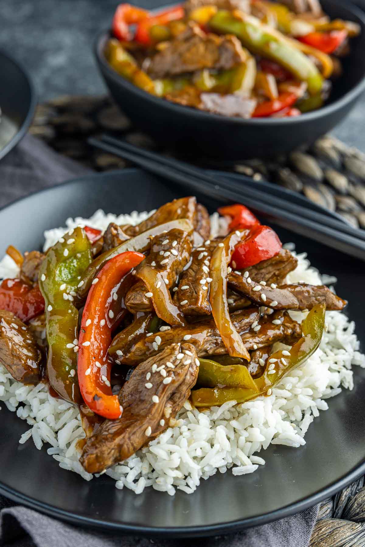 Easy Pepper Steak on a black plate with chopsticks with a bowl of Easy Pepper Steak