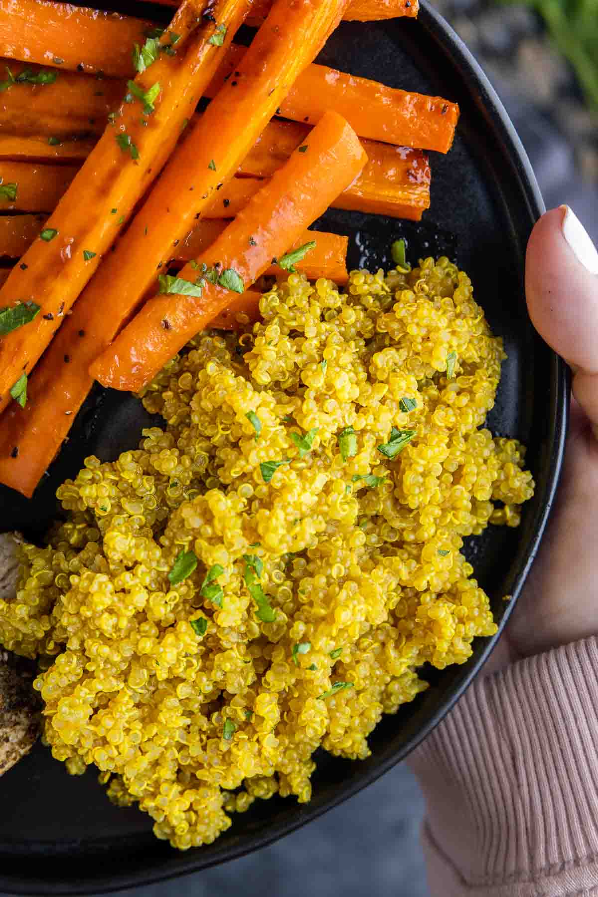 holding a black plate with Turmeric Quinoa and carrots