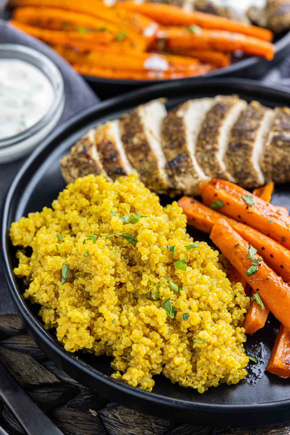 Turmeric Quinoa on a black plate with carrots and sliced chickem