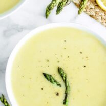 Two bowls of soup with asparagus and lemon.