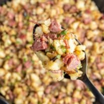 A spoonful of ham and potatoes in a skillet.