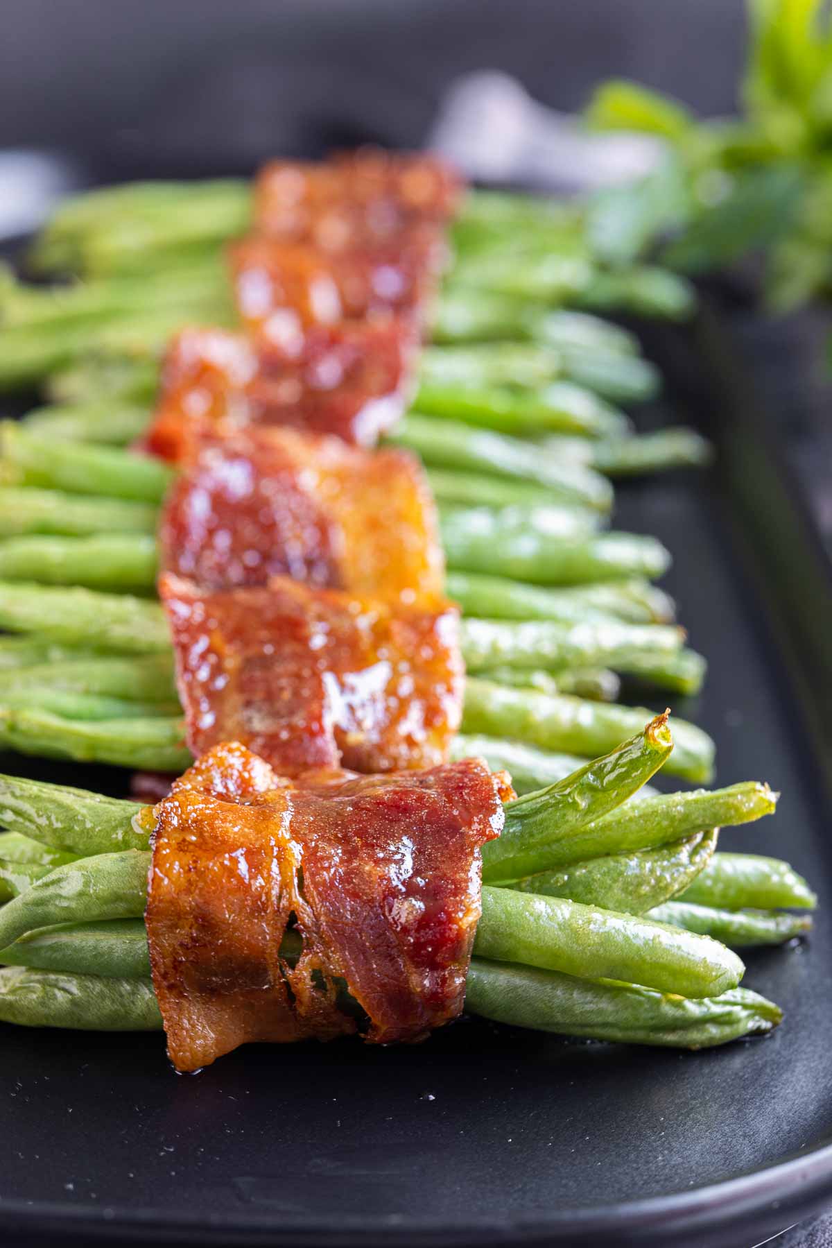 Bacon Wrapped Green Beans lined up on a black platter with parsley in the background