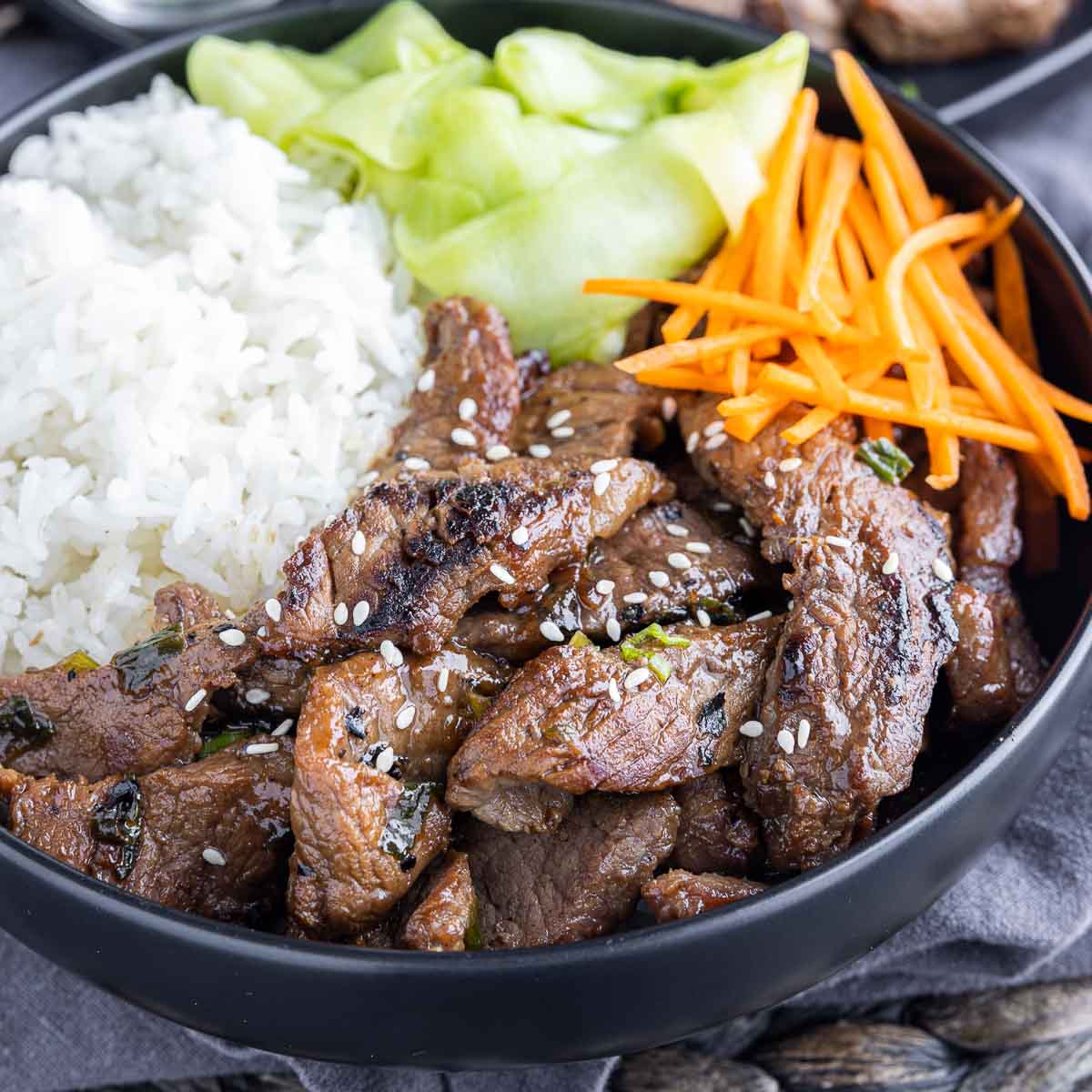black bowl of Beef Bulgogi with rice, cucumbers and carrots
