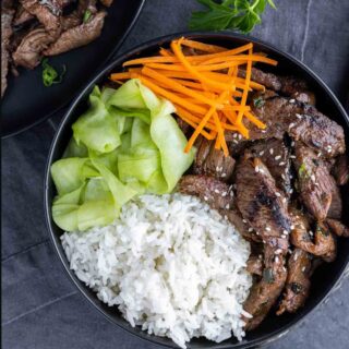 top down of beef bulgogi in a black bowl with rice and vegetables