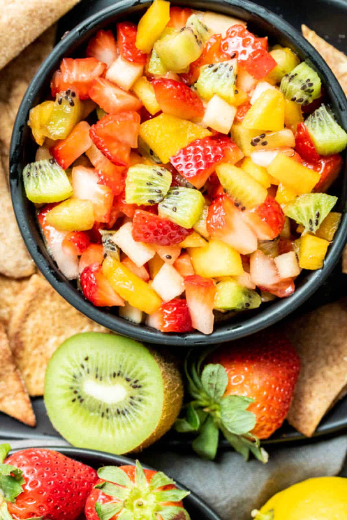 top down shot of fruit salsa in a black bowl surrounded by whole fruit